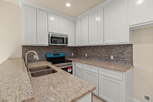 kitchen with appliances with stainless steel finishes, white cabinetry, sink, backsplash, and light stone counters