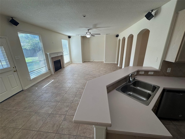 kitchen with dishwasher, ceiling fan, sink, a fireplace, and a textured ceiling