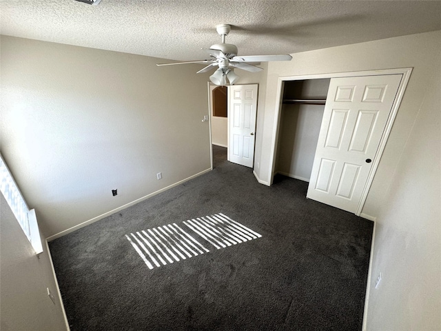 unfurnished bedroom with dark colored carpet, a textured ceiling, a closet, and ceiling fan