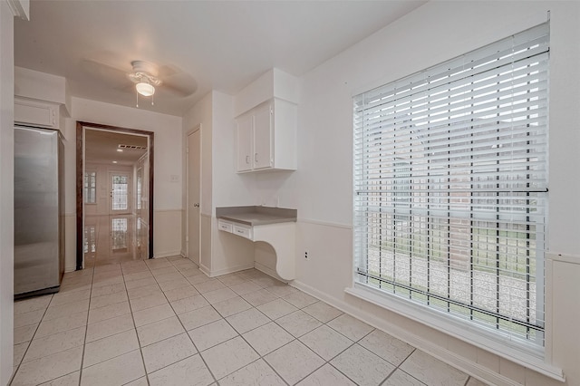 kitchen featuring stainless steel refrigerator, white cabinetry, built in desk, and light tile patterned floors