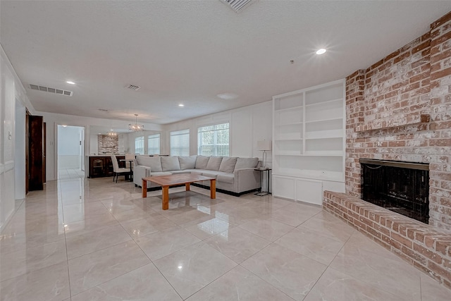 living room featuring an inviting chandelier, a brick fireplace, built in shelves, and a textured ceiling