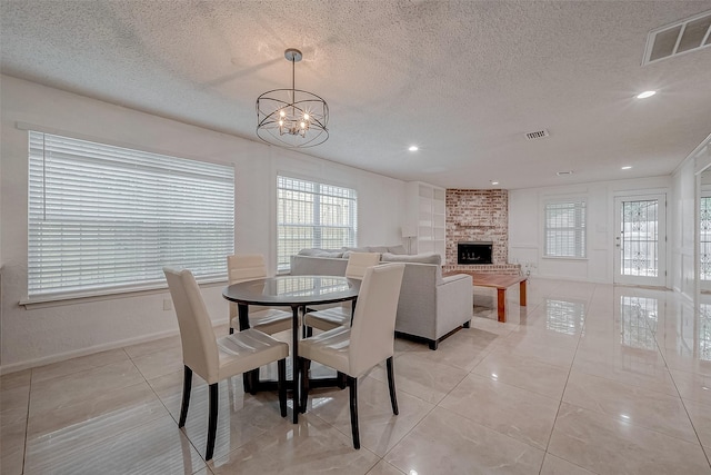 tiled dining room with an inviting chandelier, a large fireplace, a textured ceiling, and a wealth of natural light