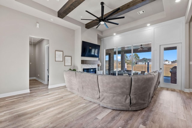 living room with a fireplace, light wood-type flooring, beamed ceiling, and ceiling fan