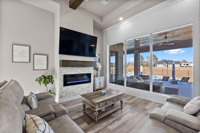 living room with ceiling fan, hardwood / wood-style floors, beamed ceiling, and a stone fireplace