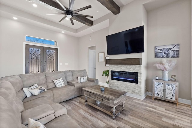 living room with beamed ceiling, light hardwood / wood-style floors, a fireplace, a high ceiling, and ceiling fan