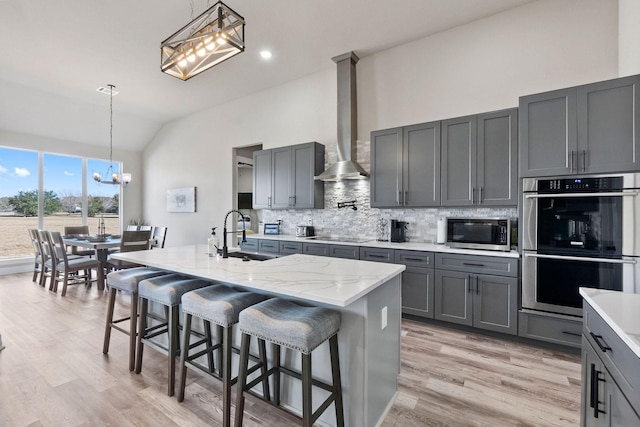 kitchen featuring appliances with stainless steel finishes, wall chimney range hood, an island with sink, sink, and vaulted ceiling