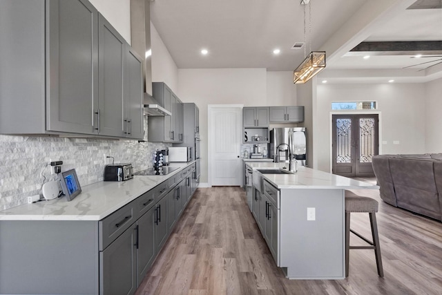 kitchen with stainless steel refrigerator with ice dispenser, gray cabinetry, a kitchen island with sink, a breakfast bar, and black electric cooktop