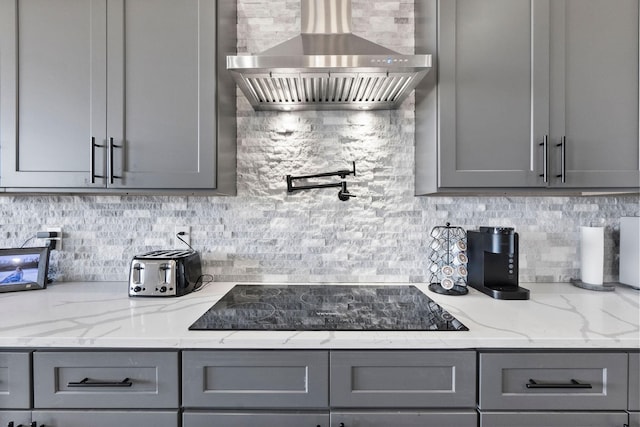 kitchen with light stone countertops, gray cabinets, wall chimney exhaust hood, and tasteful backsplash