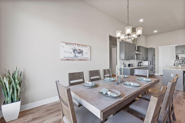 dining space with sink, a high ceiling, an inviting chandelier, and light hardwood / wood-style floors