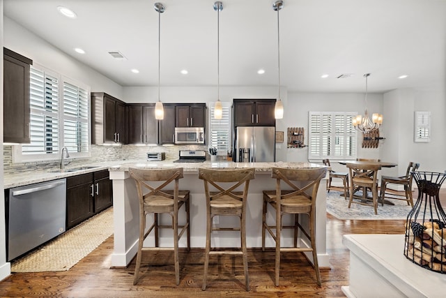 kitchen featuring dark brown cabinetry, stainless steel appliances, a sink, a center island, and decorative light fixtures