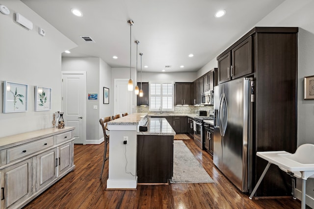 kitchen featuring light stone counters, a breakfast bar area, appliances with stainless steel finishes, a center island, and dark wood finished floors