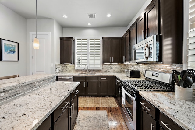 kitchen with dark brown cabinetry, a sink, visible vents, appliances with stainless steel finishes, and decorative light fixtures