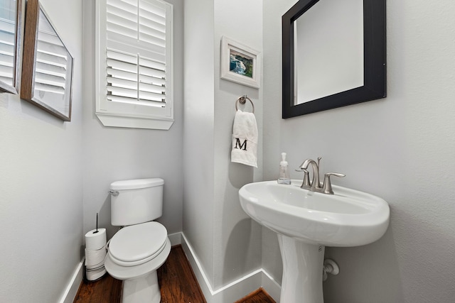 half bath with toilet, baseboards, and wood finished floors