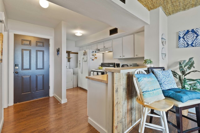 kitchen with kitchen peninsula, dark hardwood / wood-style flooring, washing machine and clothes dryer, white appliances, and white cabinets