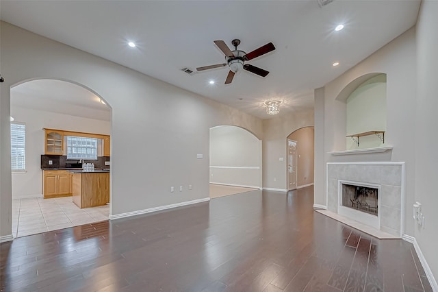 unfurnished living room with a tiled fireplace, light hardwood / wood-style flooring, and ceiling fan