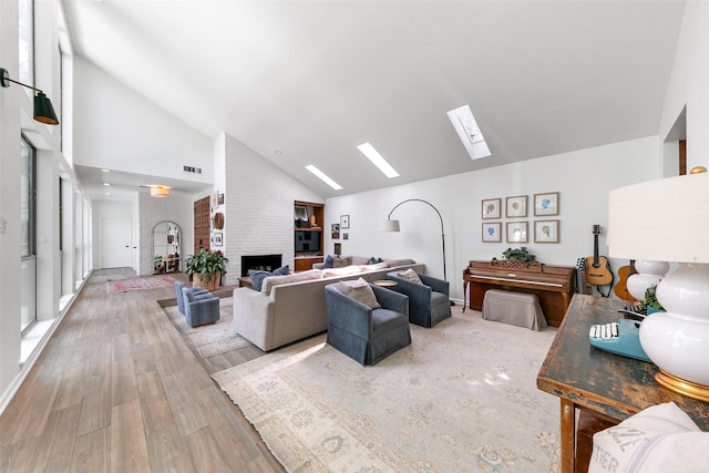 living room featuring a skylight, high vaulted ceiling, a brick fireplace, and hardwood / wood-style flooring