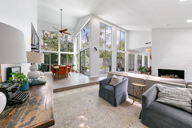 living room featuring a fireplace, light hardwood / wood-style floors, a high ceiling, and ceiling fan