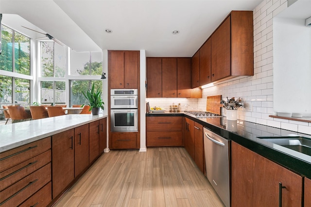 kitchen with light wood-type flooring, backsplash, appliances with stainless steel finishes, and plenty of natural light