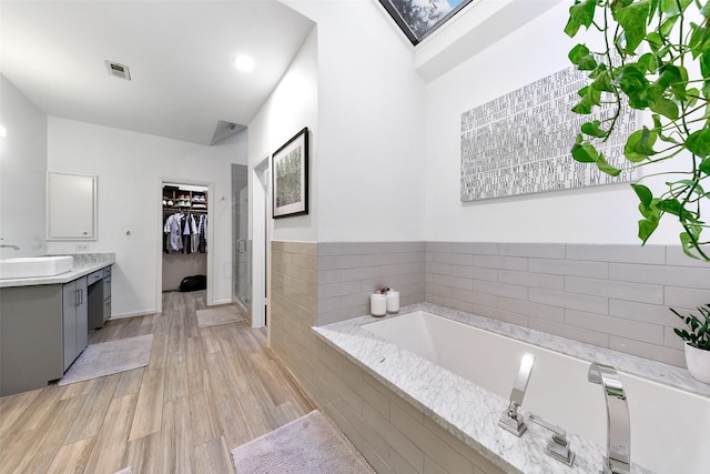 bathroom featuring wood-type flooring, a relaxing tiled tub, a skylight, and vanity