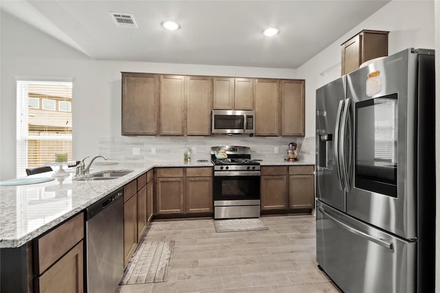 kitchen featuring sink, kitchen peninsula, stainless steel appliances, light hardwood / wood-style floors, and decorative backsplash