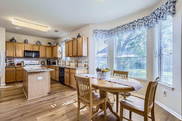 kitchen with a kitchen island, sink, black appliances, light stone countertops, and light hardwood / wood-style flooring