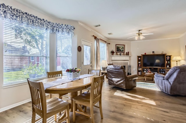 dining space featuring a healthy amount of sunlight, a fireplace, ornamental molding, and wood-type flooring