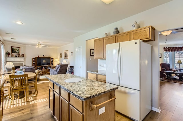 kitchen with a kitchen island, white refrigerator, ceiling fan, light hardwood / wood-style floors, and light stone countertops