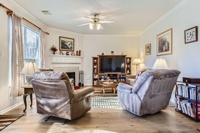 living room with crown molding, light hardwood / wood-style flooring, a tile fireplace, and ceiling fan