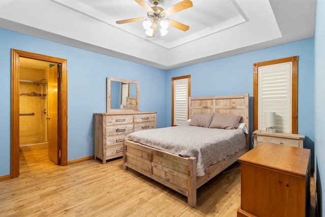 bedroom with ceiling fan, light hardwood / wood-style floors, and a tray ceiling