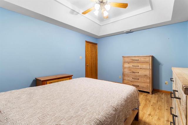 bedroom featuring light hardwood / wood-style floors, a tray ceiling, and ceiling fan