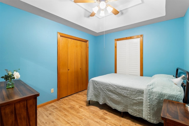 bedroom featuring light hardwood / wood-style floors, a closet, a tray ceiling, and ceiling fan