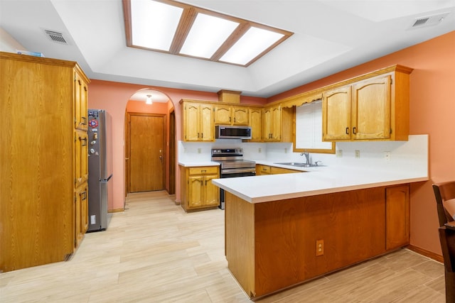 kitchen with appliances with stainless steel finishes, light hardwood / wood-style floors, sink, a raised ceiling, and kitchen peninsula