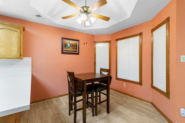 dining space with light wood-type flooring, ceiling fan, and a tray ceiling