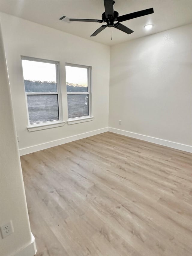 empty room with ceiling fan, a water view, and light hardwood / wood-style floors