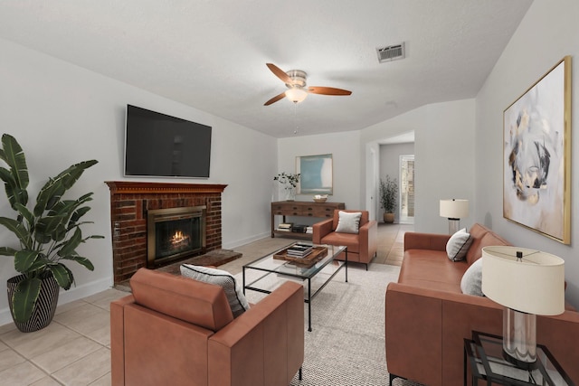 tiled living room featuring ceiling fan and a brick fireplace