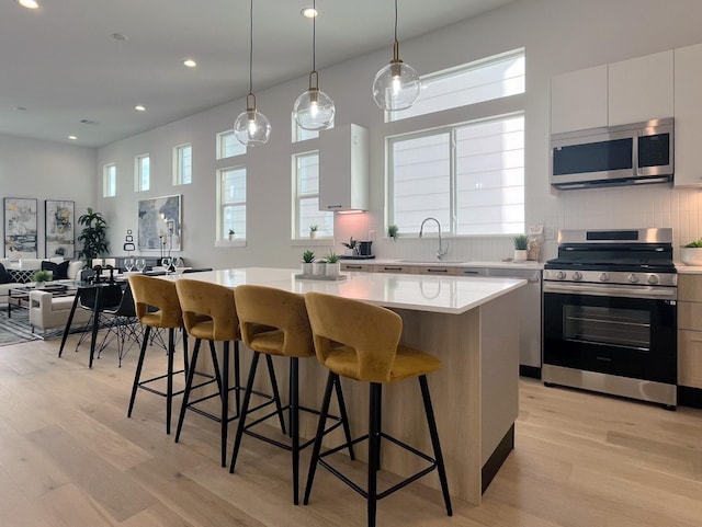 kitchen featuring decorative light fixtures, a center island, light hardwood / wood-style flooring, appliances with stainless steel finishes, and white cabinets