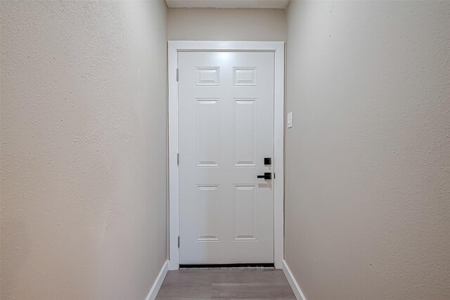 doorway to outside featuring baseboards, wood finished floors, and a textured wall