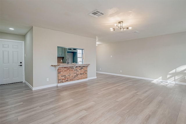 unfurnished living room featuring sink, light hardwood / wood-style floors, and a notable chandelier