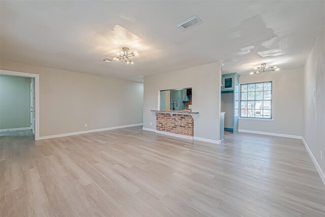 unfurnished room featuring baseboards, light wood finished floors, visible vents, and an inviting chandelier