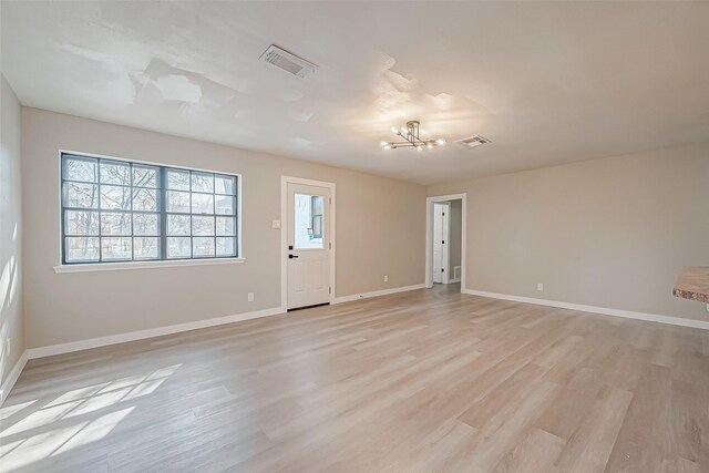 spare room with light wood finished floors, baseboards, visible vents, and an inviting chandelier