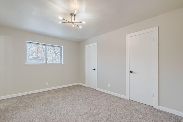 carpeted empty room featuring baseboards and an inviting chandelier