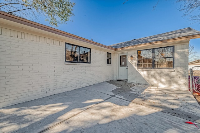 property entrance featuring a shingled roof, brick siding, and a patio