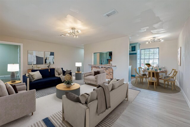 living area featuring light wood-style flooring, visible vents, a chandelier, and baseboards