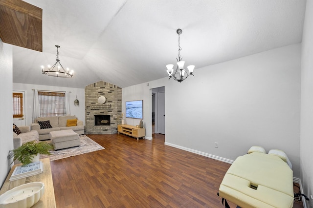 living area with dark wood finished floors, a brick fireplace, lofted ceiling, and an inviting chandelier