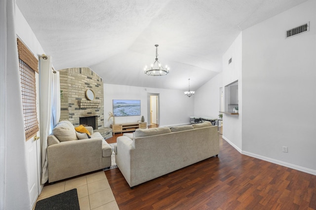 living room featuring vaulted ceiling, wood-type flooring, a chandelier, a brick fireplace, and a textured ceiling