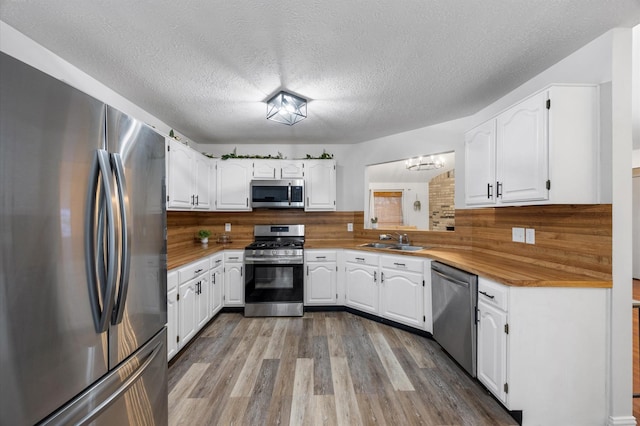 kitchen with wood finished floors, a sink, stainless steel appliances, white cabinets, and backsplash