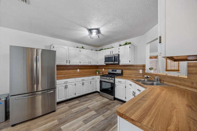 kitchen featuring a sink, white cabinets, appliances with stainless steel finishes, a textured ceiling, and light wood-type flooring