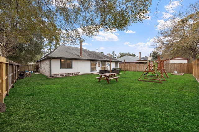 rear view of house with a yard, a shingled roof, a fenced backyard, and a playground