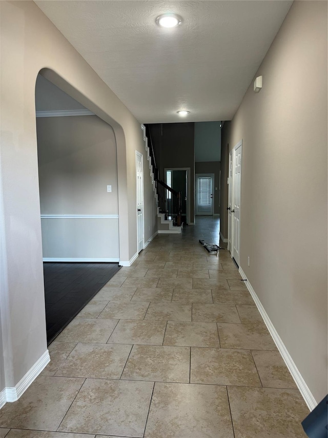 corridor featuring light tile patterned floors, stairs, baseboards, and arched walkways