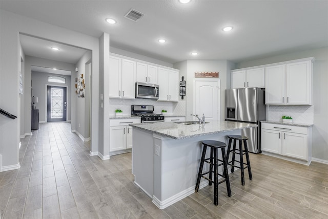 kitchen featuring white cabinets, appliances with stainless steel finishes, an island with sink, sink, and light stone counters